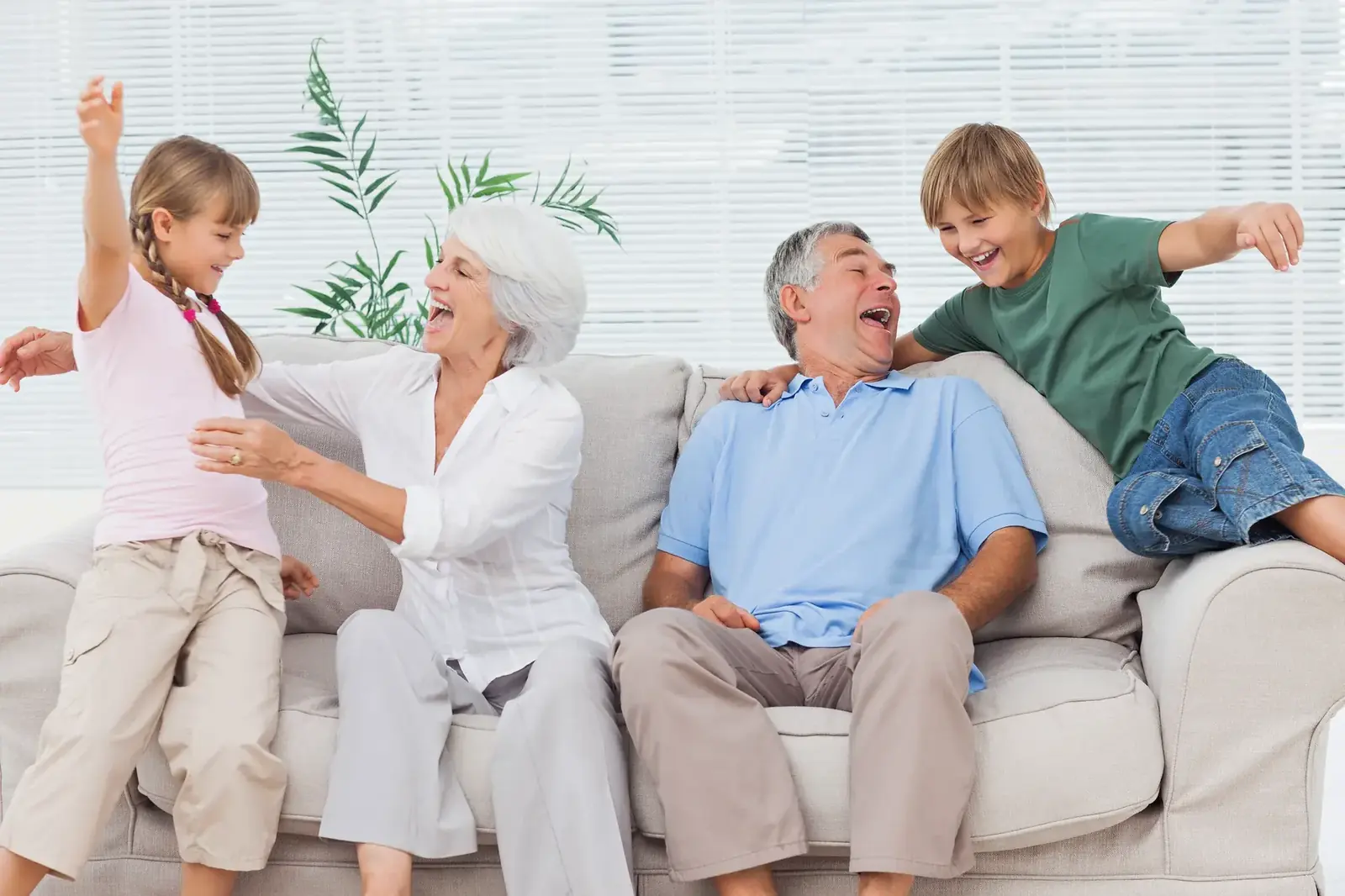 Grandparents laughing with their grandchildren on the sofa in a bright, clean living room