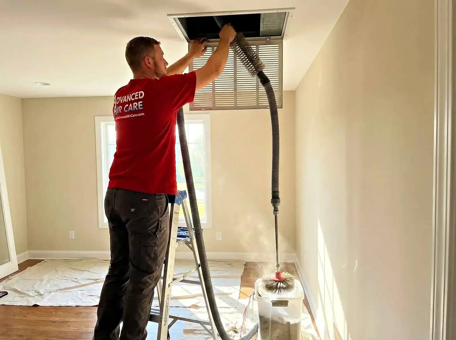Advanced Air Care technician cleaning a ceiling air duct register in a Macomb home