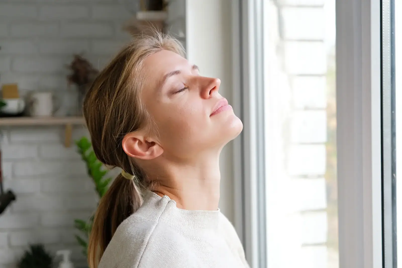 Woman breathing easy beside an open window at home